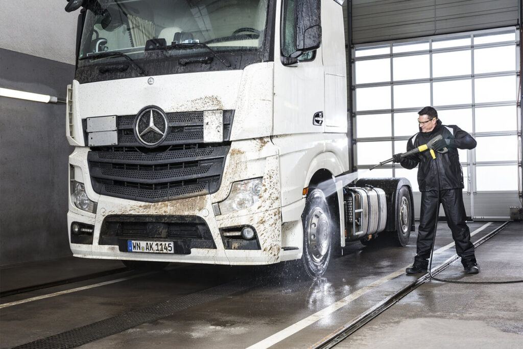 Man using pressure washer to clean dirty white truck