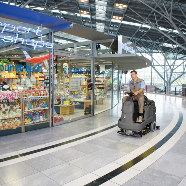 Man riding B 90 R floor scrubber in empty airport concourse