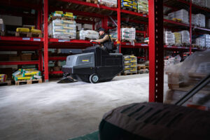 Man riding KM 105/180 R Vacuum Sweeper inside warehouse
